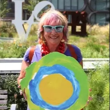 A woman with pink hair holds up the Idealist logo.