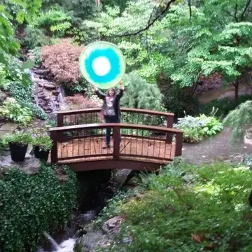 A woman on a bridge holds up the Idealist logo.