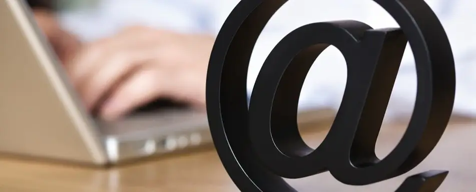 a photograph of an internet @ sign in front of someone typing on a laptop.