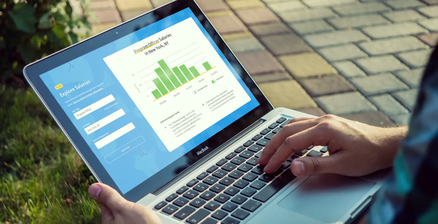 A photograph of someone sitting outside and using the Nonprofit Salary Explorer tool on a laptop.